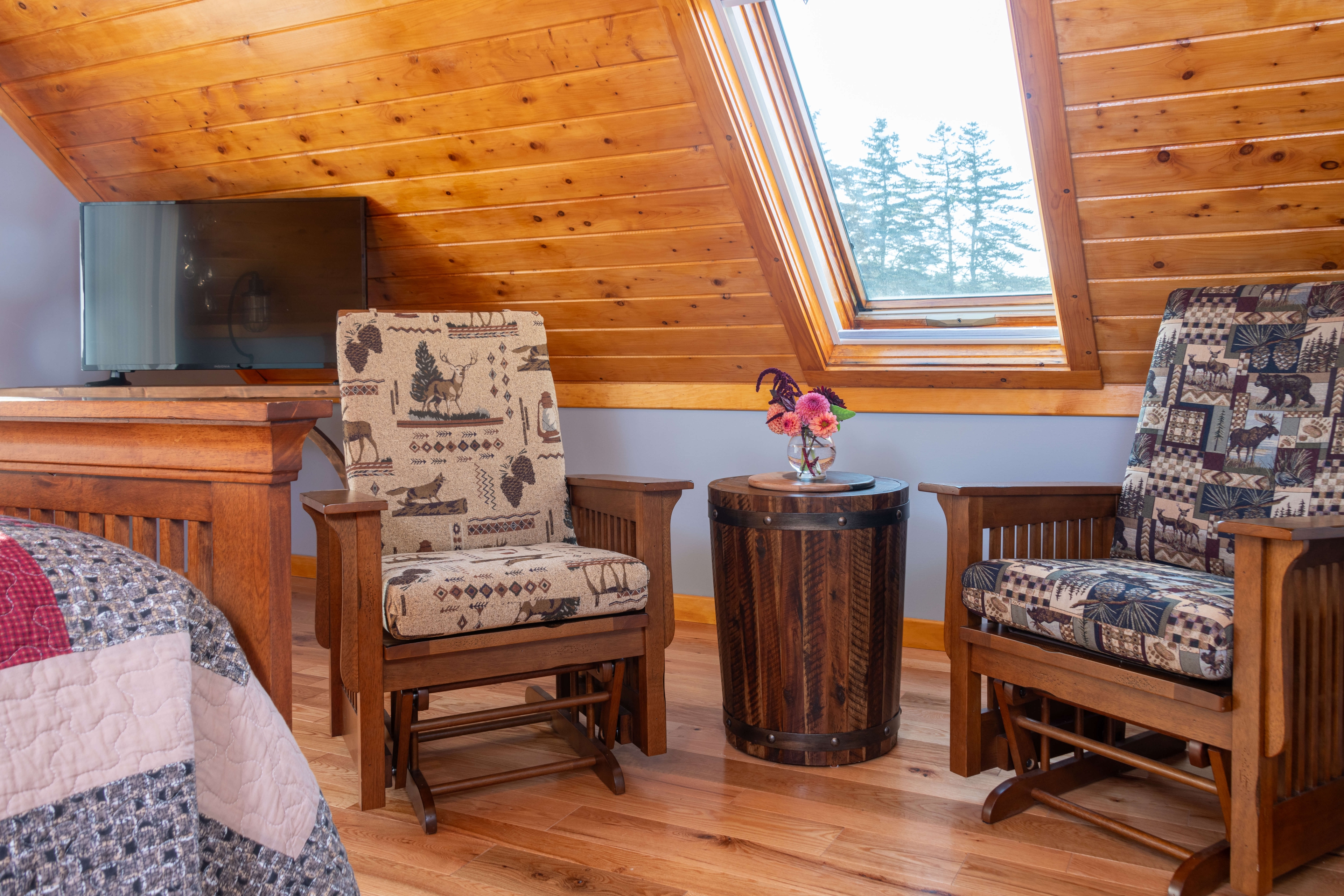 Sitting area of two rustic glider chairs and flowers in front of large window