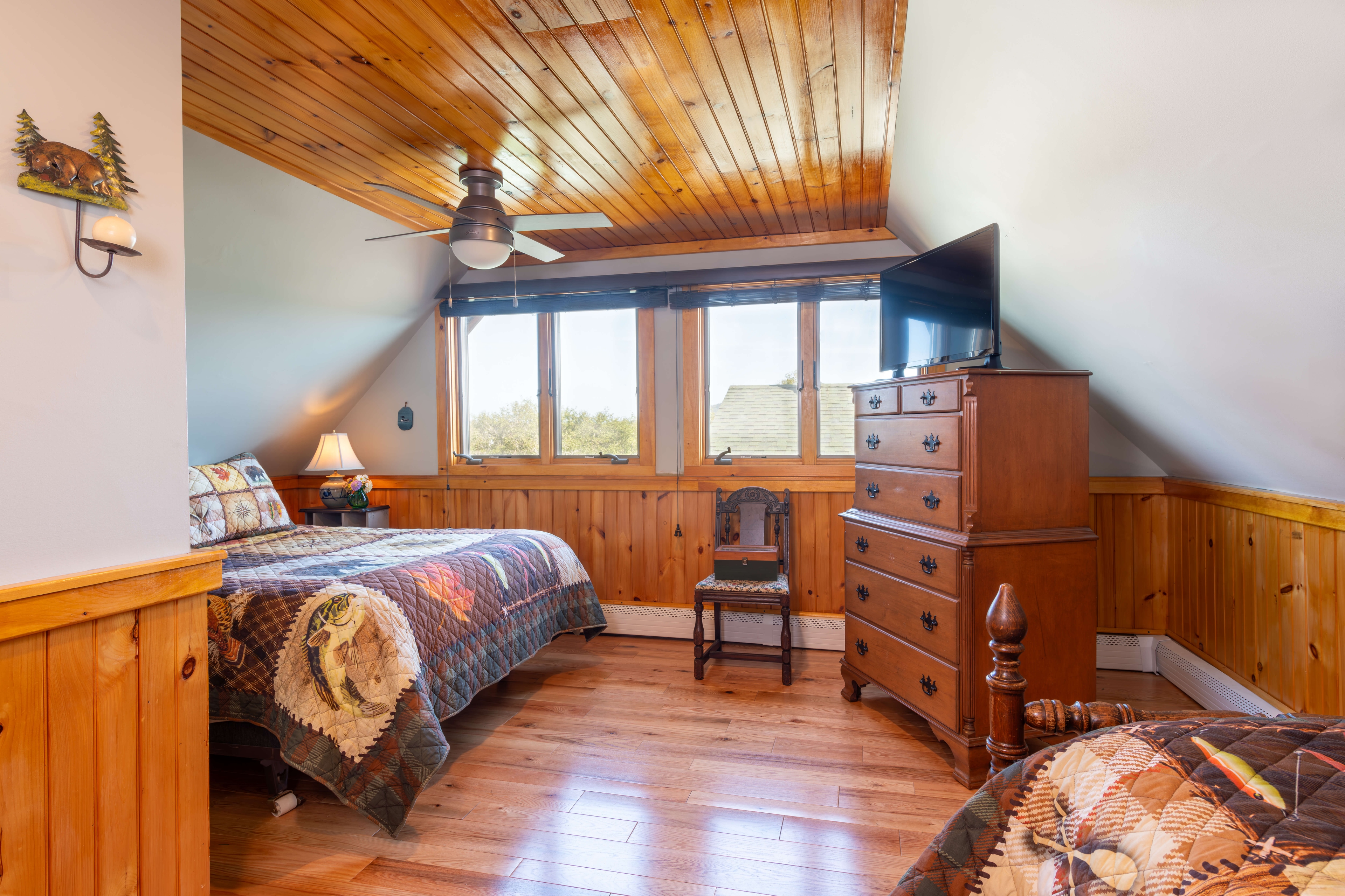 Two beds with quilted bedspreads and a wooden bureau near a bright window