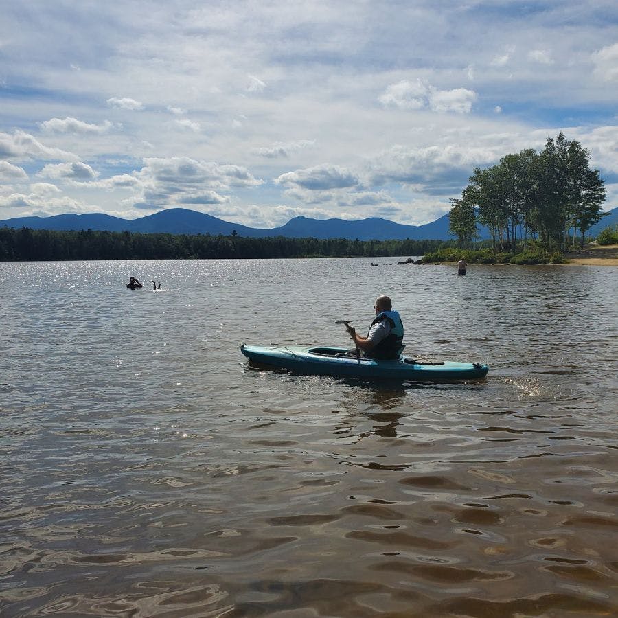 Large lake with mountains in the background, sunny skies and a kayaker out for a paddle.