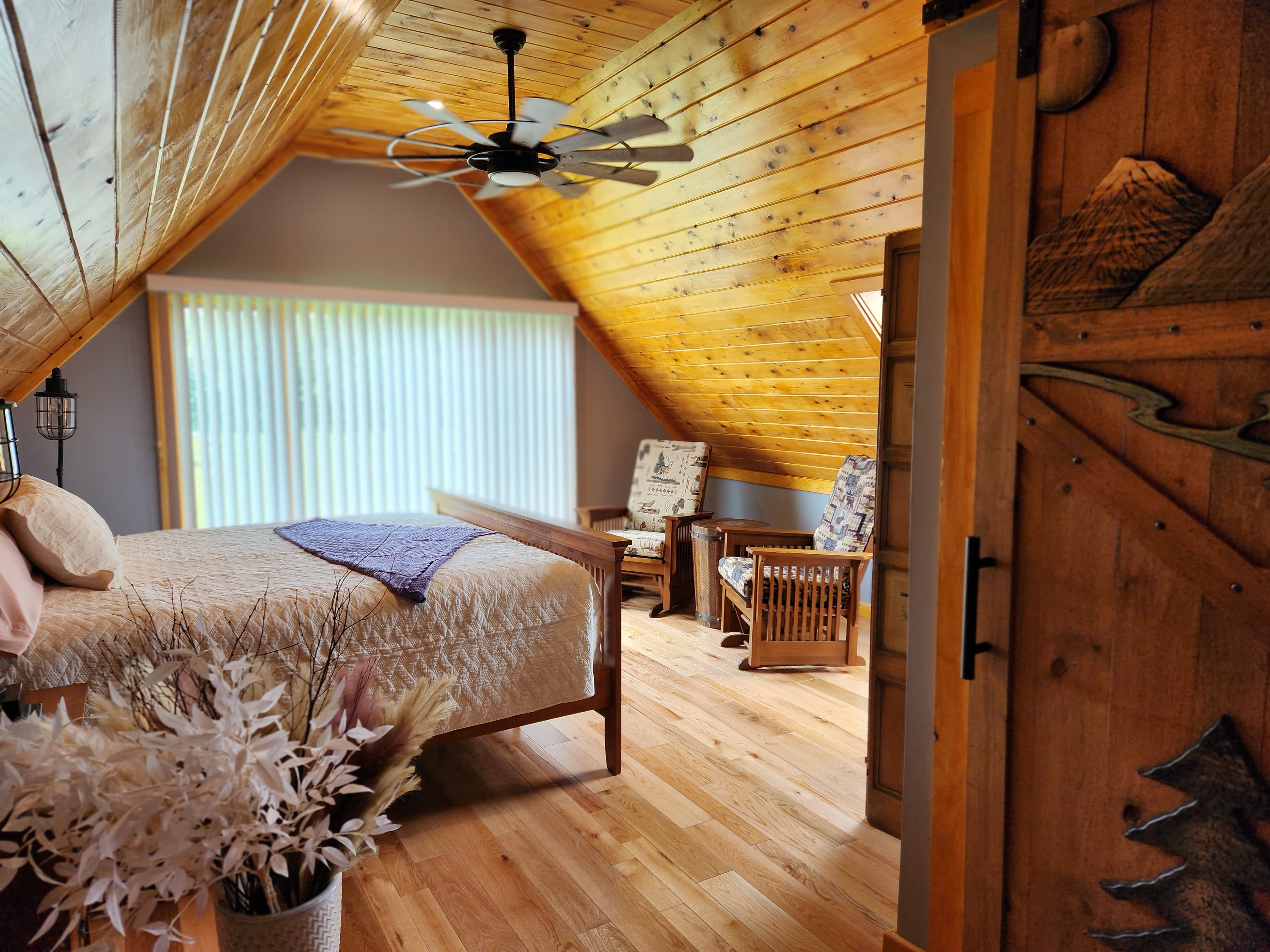 View through bedroom doorway, bed, finished wood ceiling with ceiling fan, glider rockers