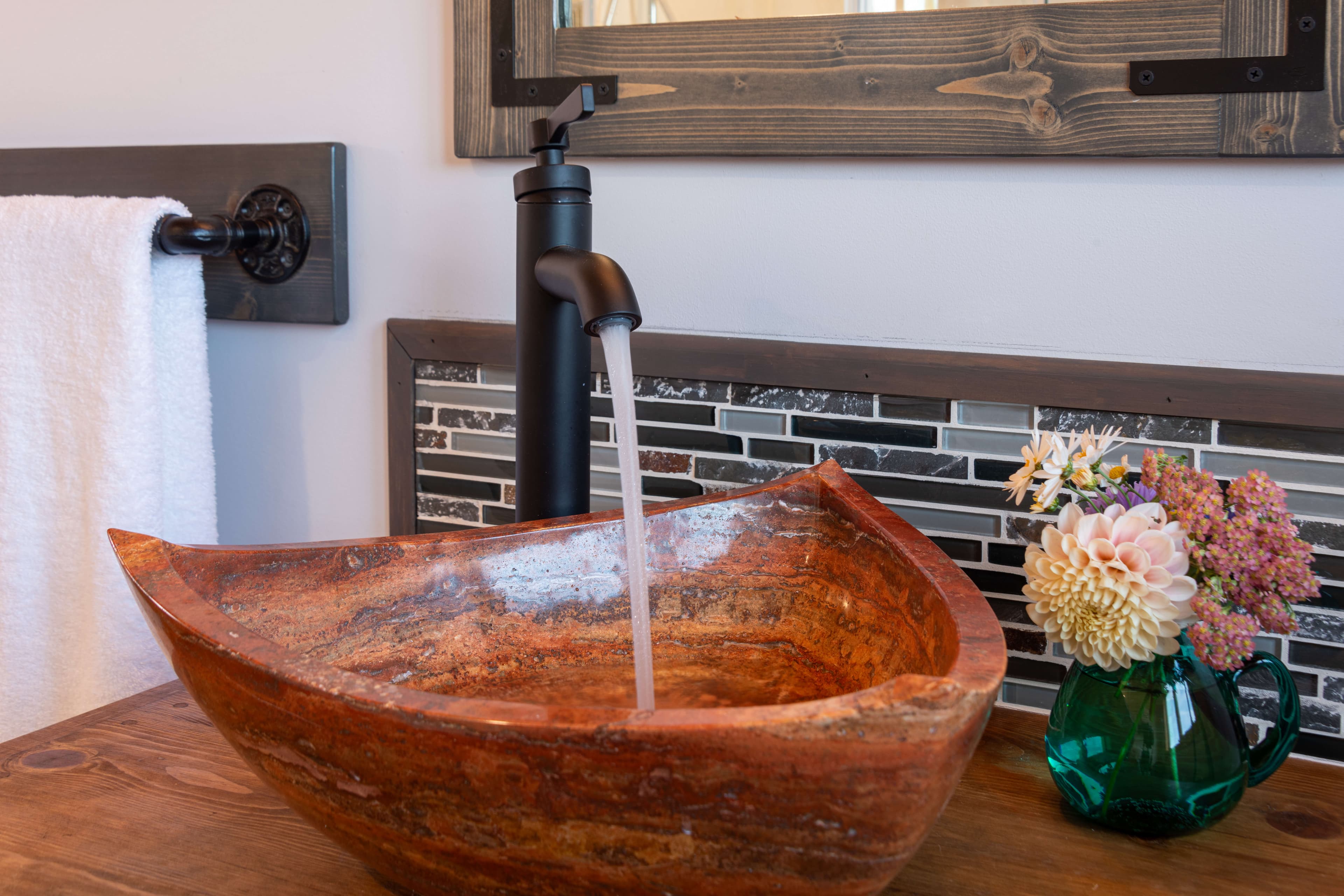 Vessel sink with running water and tiled backsplash, pitcher of fresh flowers