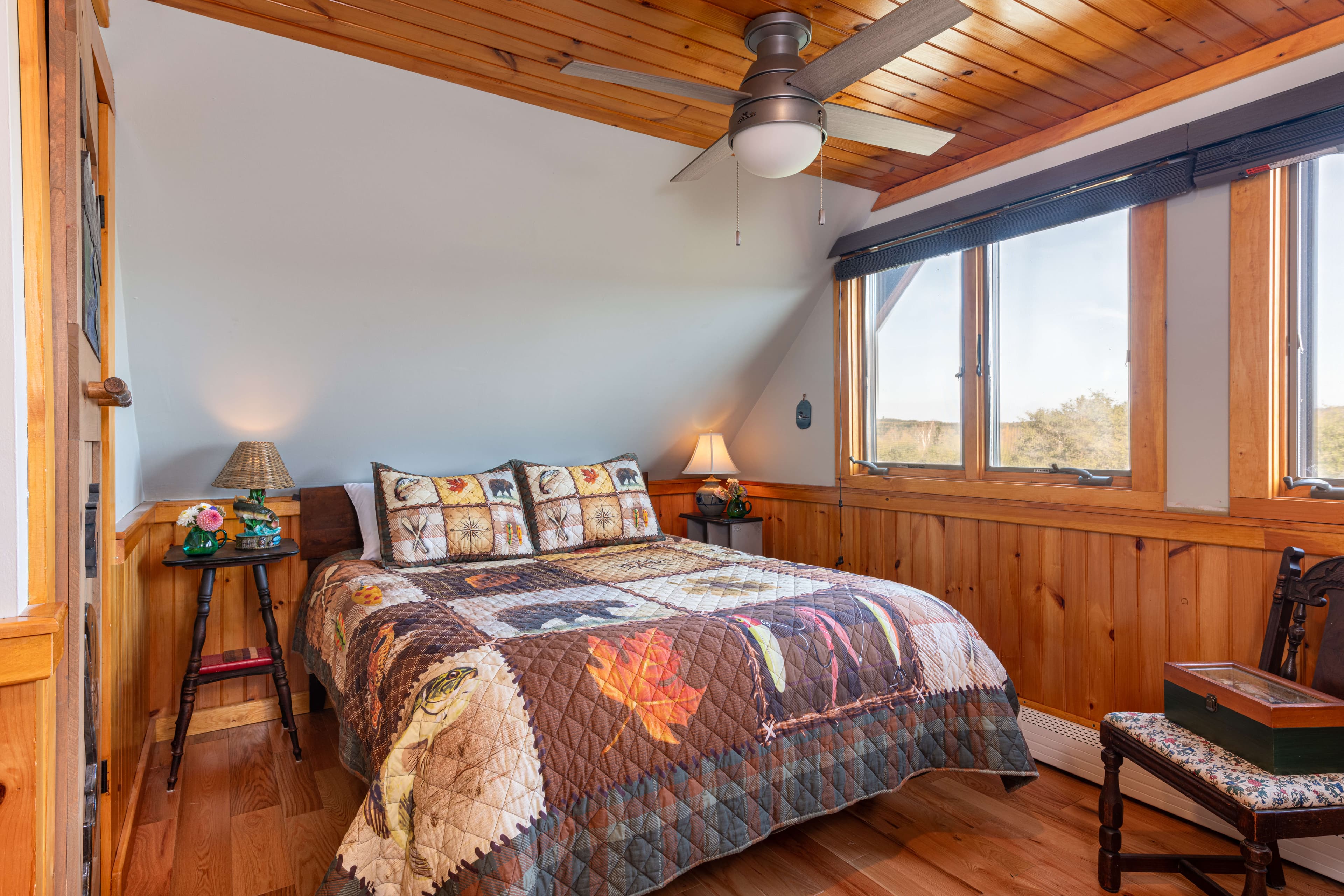 Twin bed with rustic-patterned quilt, nightstands with lamps, wooden floor & ceilings with fan