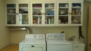 White cupboards with glass doors hanging over washer and dryer in a laundry area