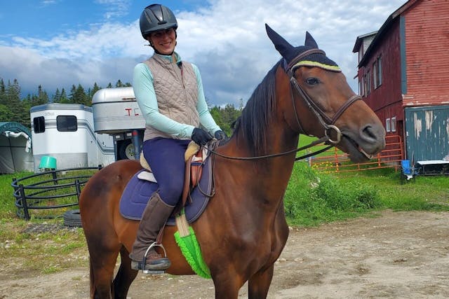 A woman wearing a helmet riding a brown horse  with trailers behind