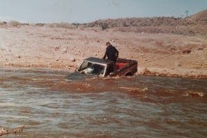 A man in the bed of a truck that is being pulled out of a river.