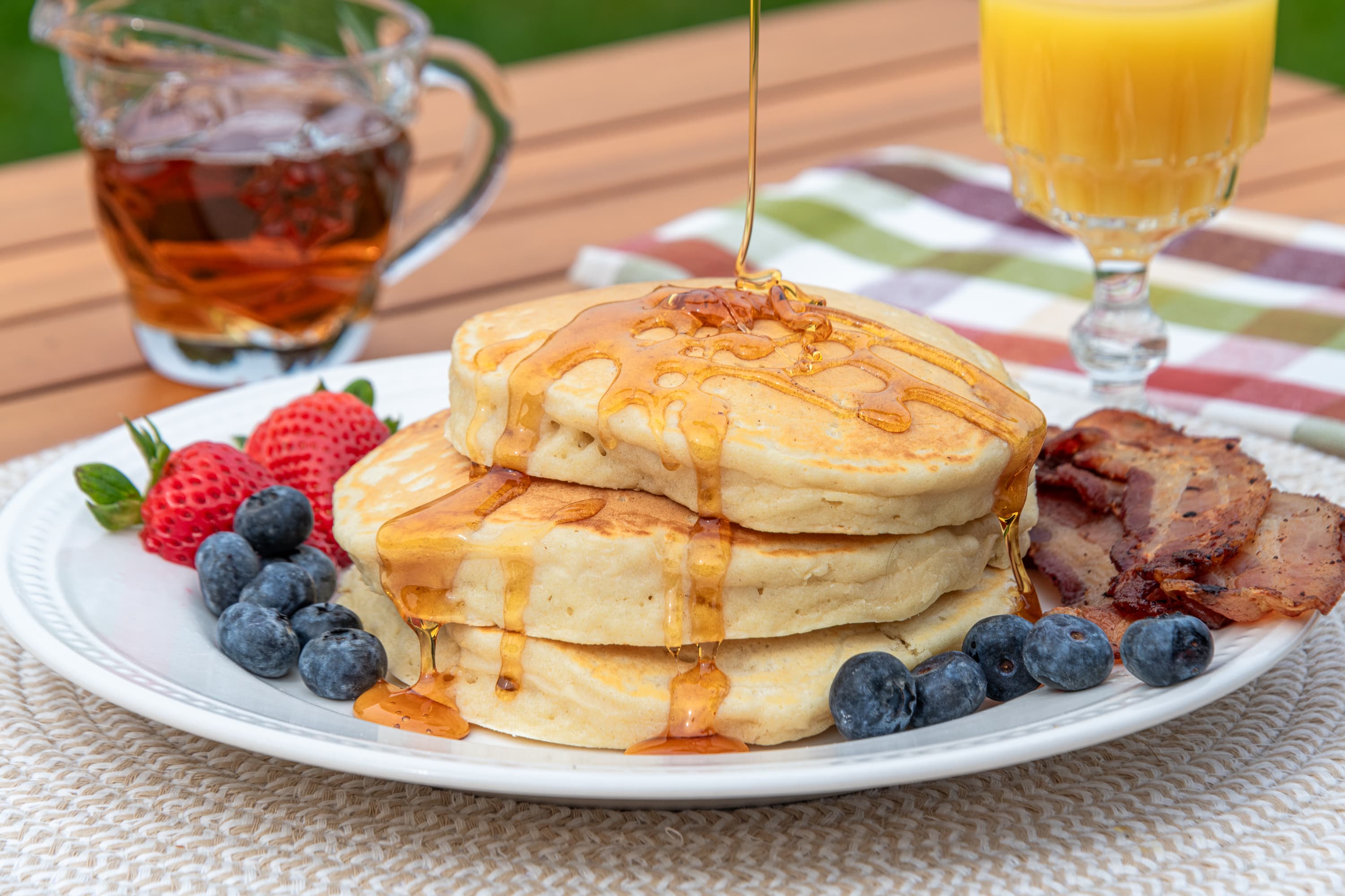 pancakes  with syrup, bacon strawberries, blueberries and a glass of orange juice on an outdoor table