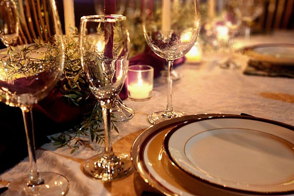 An elegant table set for dinner with white tablecloth, china plates, wine glasses, and votive candles.