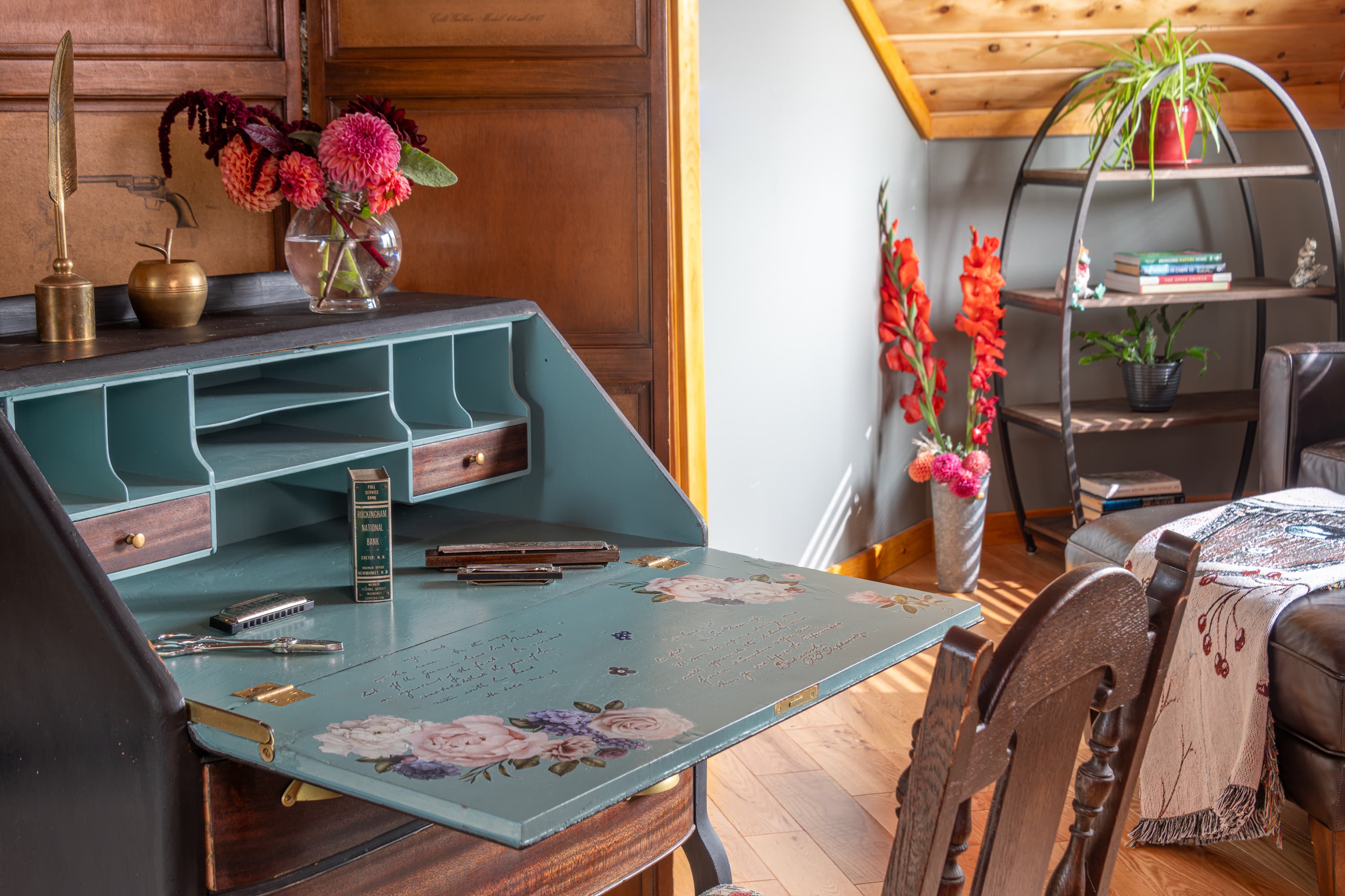 An open blue writing desk, with shelving in the corner, and flowers decorating the space