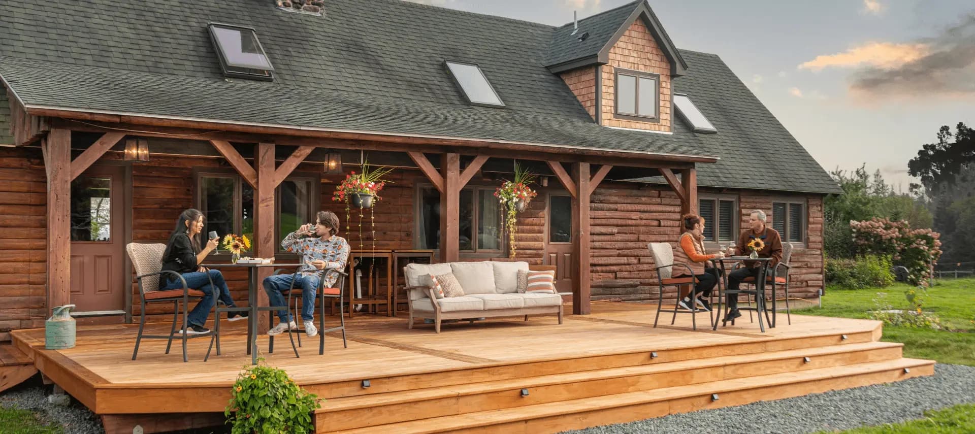 Front view of a large log cabin home with a greenhouse feature by the front door, expansive lawn, with lots of trees and bushes