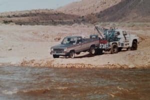A pickup truck being towed near a riverbank in a dry, rocky landscape.