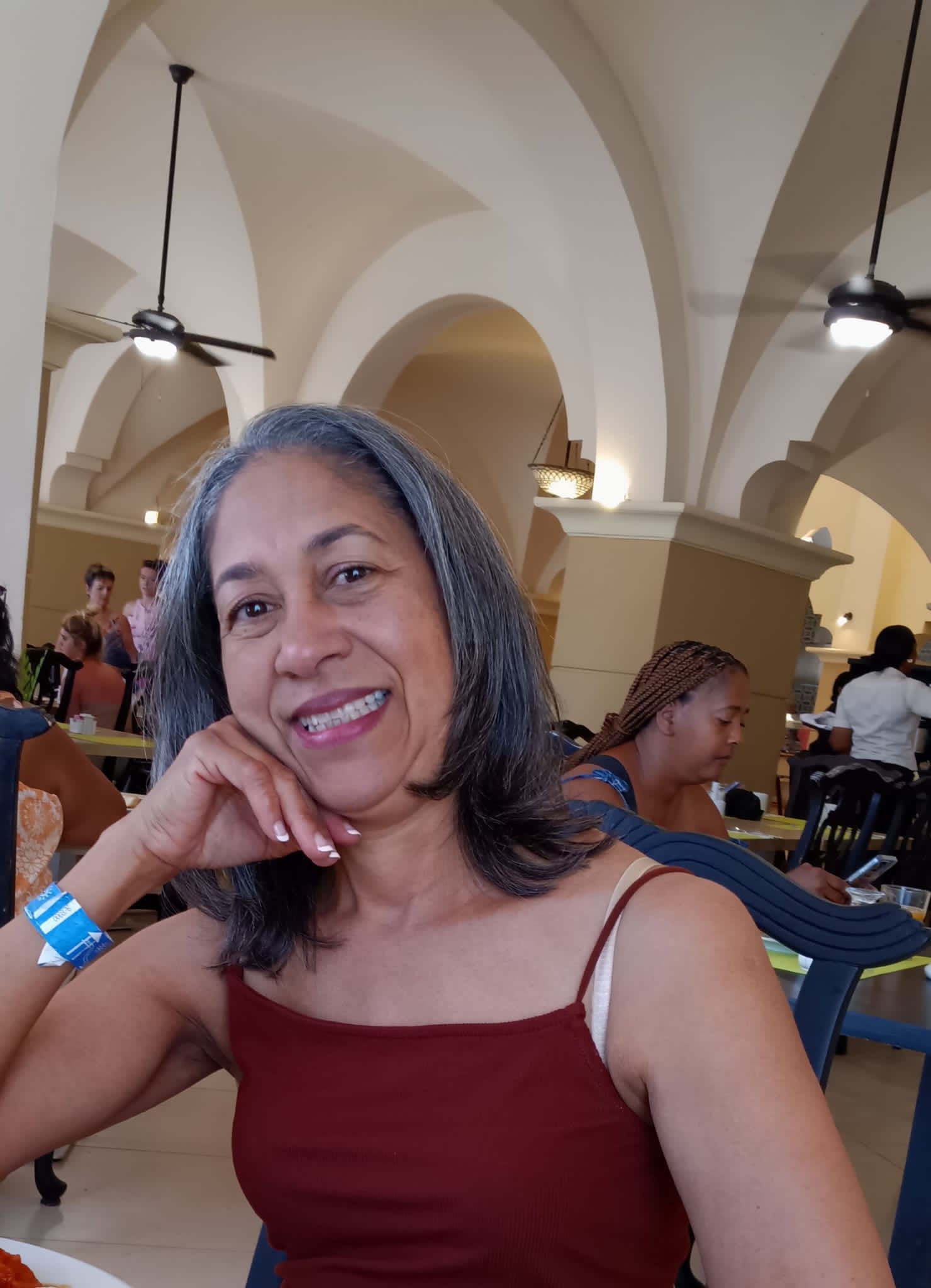 A woman with long gray hair smiles while sitting at a restaurant table.